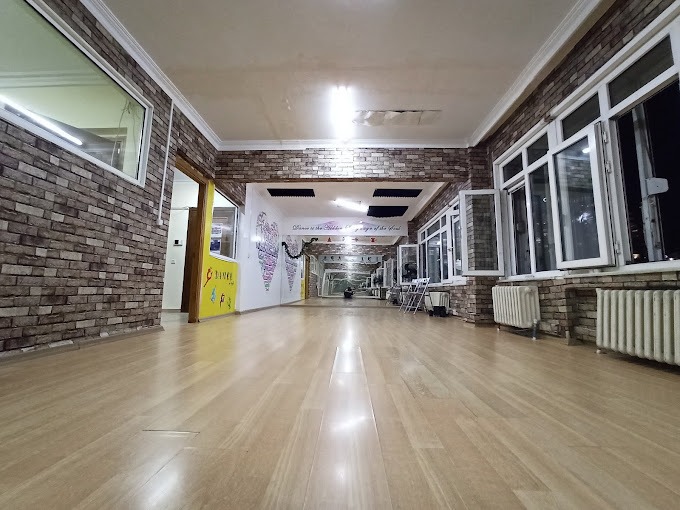 An inviting exterior shot of the 'Dance' studio location. The building should look welcoming and easy to find. Clear signage with the business name is visible. There are green plants, and perhaps dancers entering or exiting. The image should convey a sense of warmth and community.